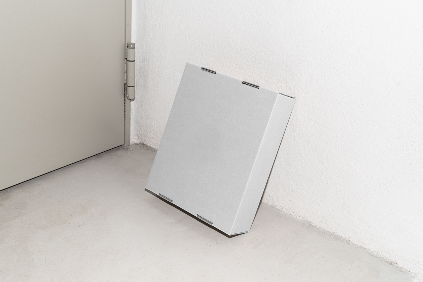 Front view, of a white cardboard box mockup based on a white wall and standing on the concrete floor.