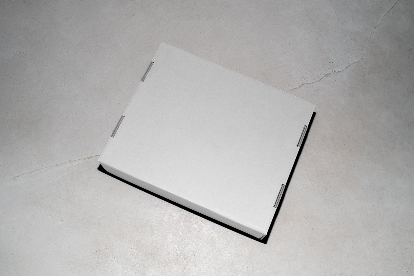 View from above of a white cardboard box mockup laying on the concrete floor.