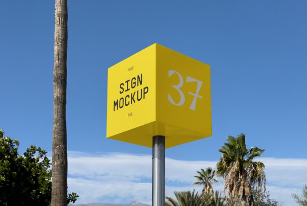 Front view, yellow square sign mockup standing between trees with a visible sky behind.