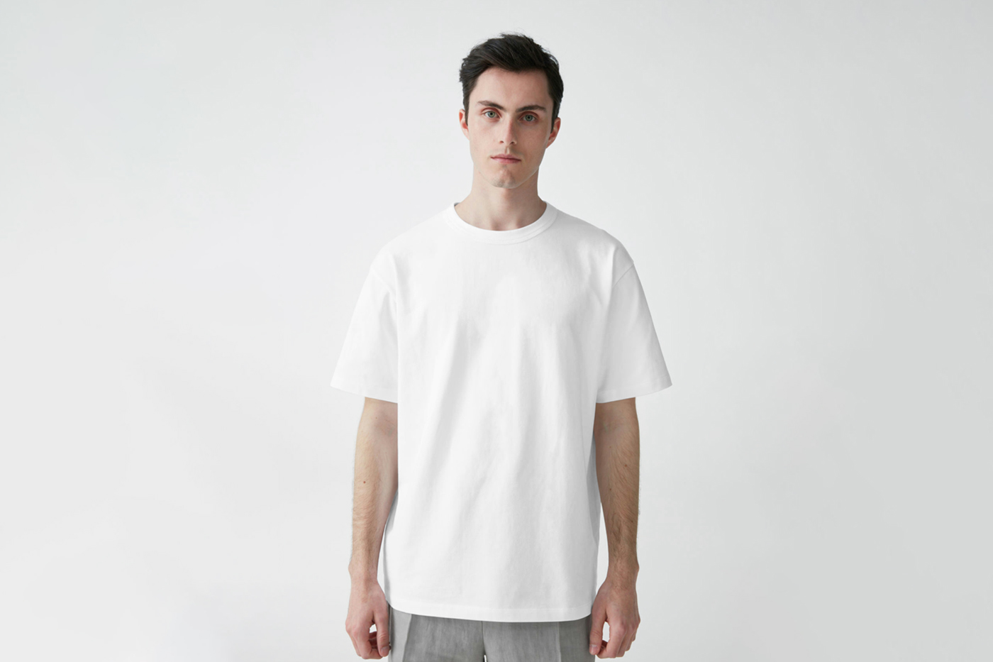 Standing men wearing blank t-shirt with in front of the white wall.