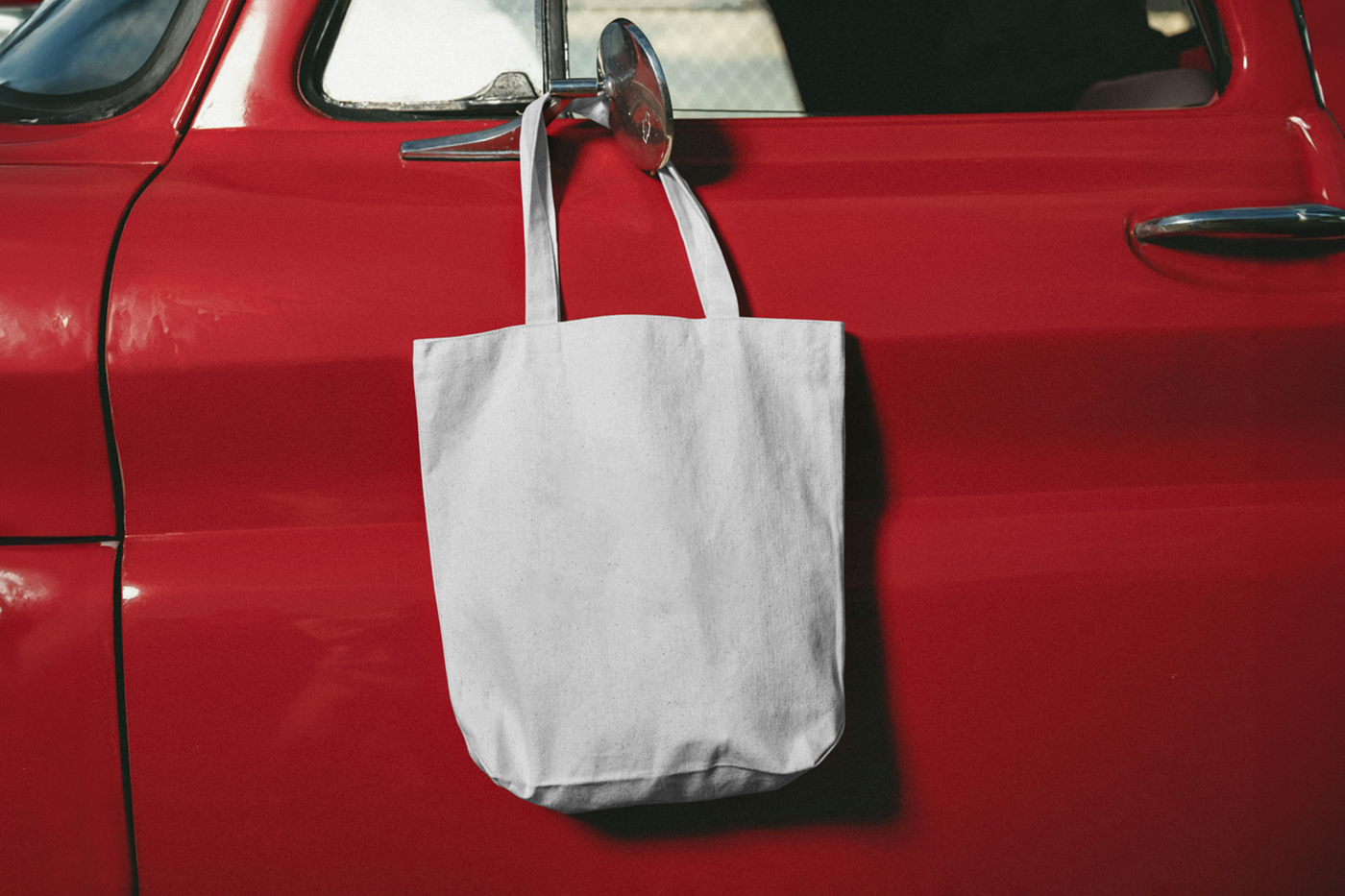 Front view, white canvas bag mockup hanging on the car's red color body.