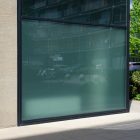 Front view, at an angle of 45 degrees, building corner from storefront mockups product with windows where you can see the reflection of city life. Behind the corner are trees, cars, and another building.