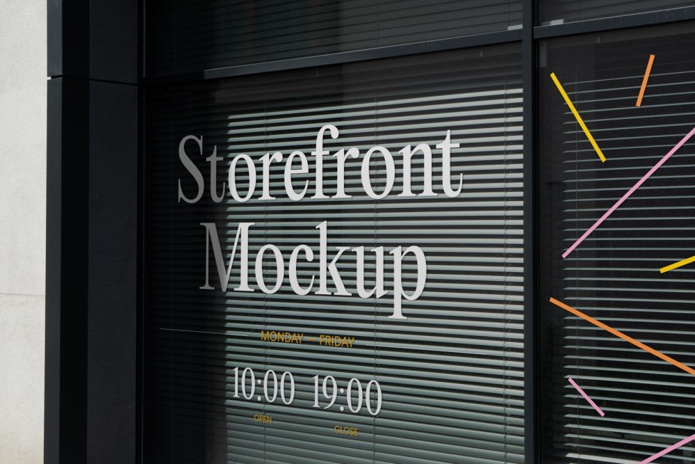 Front view, at an angle of 45 degrees, clean glass window with visible blinds behind the glass and colorful graphics, white typography from storefront mockups product.