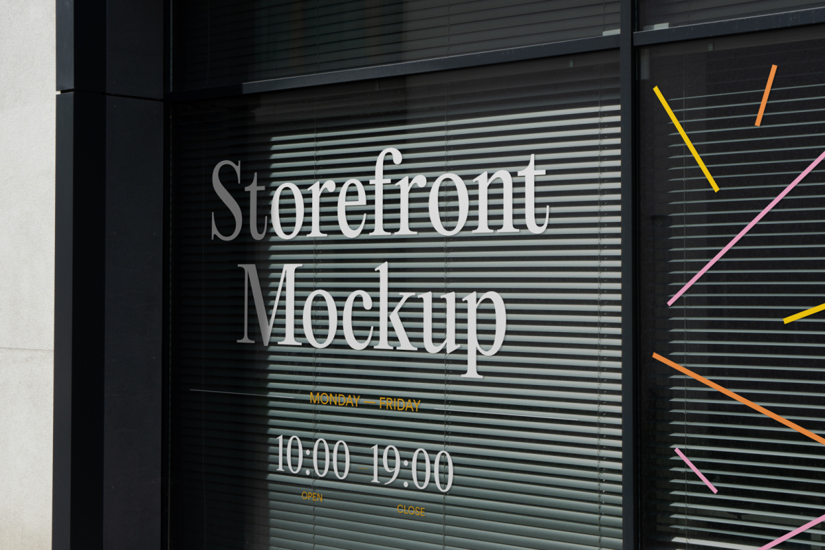 Front view, at an angle of 45 degrees, clean glass window with visible blinds behind the glass and colorful graphics, white typography from storefront mockups product.