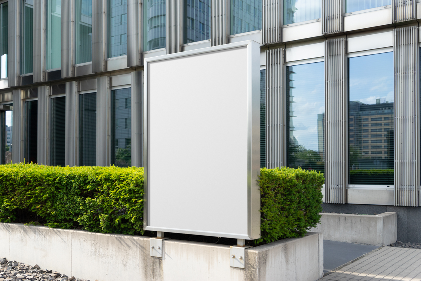 Front view, white billboard mockup with silver color metal frame attached to the concrete fence in front of the building.