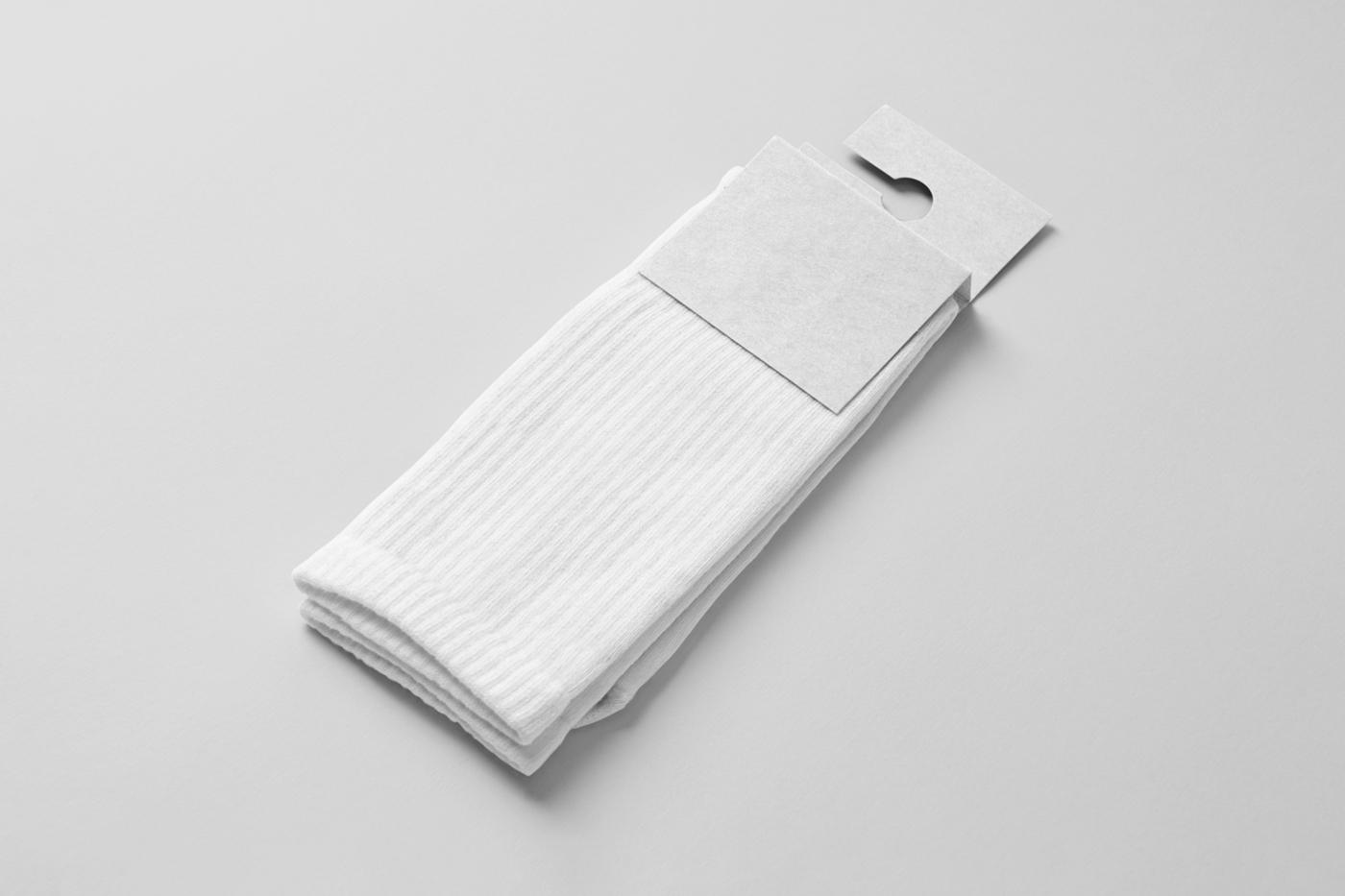 View from above, a blank pair of socks mockup with a white paper label attached to it, laying on the white floor.