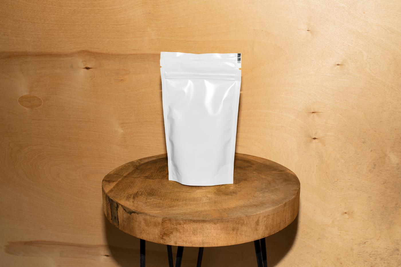 Front view, white coffee bag mockup standing on the wooden stool in front of the wooden wall.