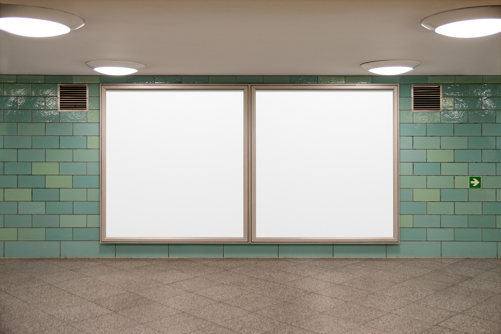 Front view, two white square city billboard mockups with silver frames attached to the green wall tiles.