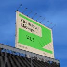 A horizontal city billboard mockup attached to the roof of the building, with the clean blue sky in the background.
