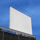 White city billboard mockup attached to the roof of the building, with the clean blue sky in the background.