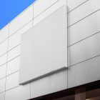 Horizontal white city billboard mockup with white coffer attached to the bright gray building facade.