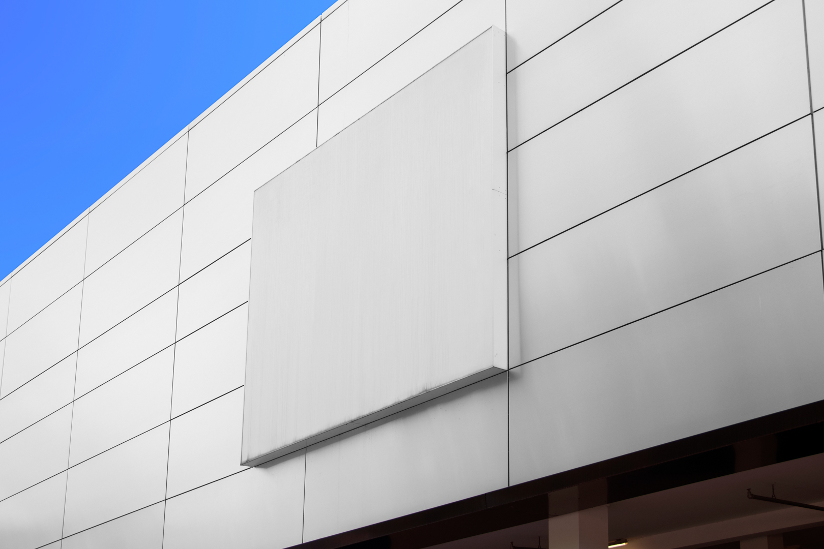 Horizontal white city billboard mockup with white coffer attached to the bright gray building facade.
