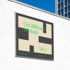 Square city billboard mockup with a dark gray, green design and silver metal frames attached to the white wall facade.
