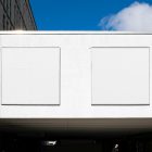 Front view, two white square city billboard mockups attached to the white wall facade.