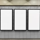Three white vertical city billboard mockups with black frames attached to the gray color wall tiles.