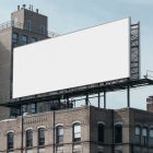 A white city billboard mockup attached to the roof of the building, with the clean blue sky in the background.