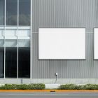 Front view, two white horizontal city billboard mockups with silver frames attached to the gray building elevation.