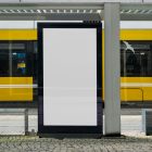 A white city billboard mockup with strong black frames attached to the bus stop with a city tram view in the background.