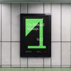 Vertical city billboard mockup with green and black design and black strong frame attached to the gray wall.