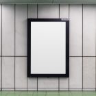 Vertical white city billboard mockup with black strong frame attached to the gray wall.