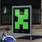 City billboard mockup with green, black design and strong silver frames standing between the buildings in the middle of the city in the background.