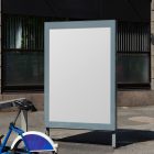 White city billboard mockup with strong silver frames standing between the buildings in the middle of the city in the background.