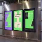 Three vertical city billboard mockups with green, purple, and black design with black frames attached to the silver metallic wall.