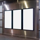 Three white vertical city billboard mockups with black frames attached to the silver metallic wall.