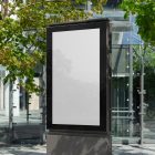 White city billboard mockup standing pedestal between the buildings in the middle of the city in the background.