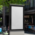 White city billboard mockup standing pedestal between the buildings in the middle of the city in the background.