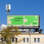 Front view, city billboard mockup attached to the roof of the building, with the clean blue sky in the background.