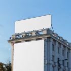 Front view, two white city billboard mockups attached to the building elevation, with the clean blue sky in the background.