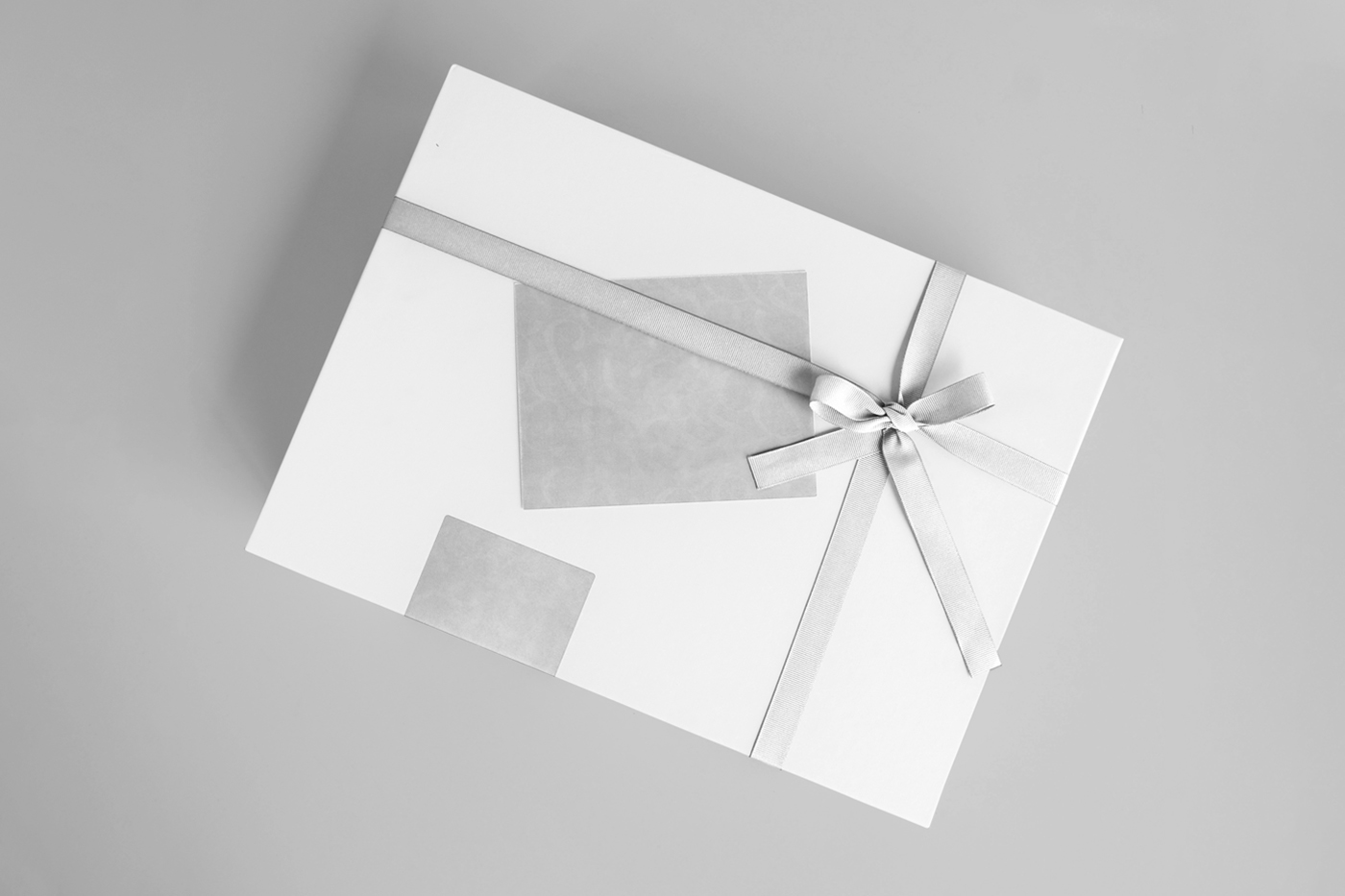 View from above, white gift box mockup with gray ribbon laying on the gray floor.