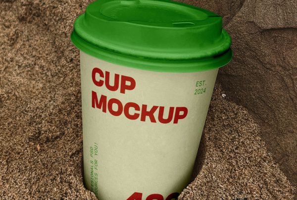 View from above, paper coffee cup mockup buried in the sand.