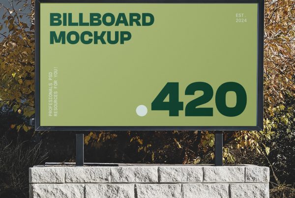 Front view, middle size green billboard with a black metal frame attached to the bright brick construction in front of the trees.