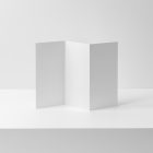 Front view, of a white Trifold Mockup standing on a white box, where behind is a white wall.