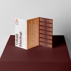 Front view, from above, with a little angle of single standing on a dark claret box Trifold Mockup arranged in the letter z. Behind the claret box is a huge white wall.