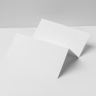 Front view, of a white Trifold Mockup arranged in the letter z and laying on a white box. Behind the white box is a huge white wall.