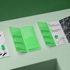 View from above, at a 45-degree angle of a three Trifold Mockups laying on a light green box. Two of them are opened and showing what is inside.