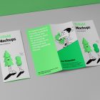 View from above, at a 45-degree angle of a two Trifold Mockups laying on a light gray box. One is close and showing green graphic illustration with typography. The second is opened and shows what is inside the brochure.