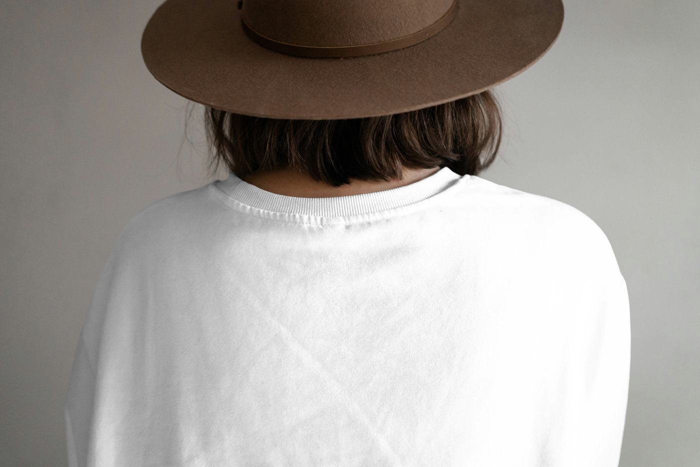 Front view, standing woman backwards wearing t-shirt mockup right in front of the gray wall.