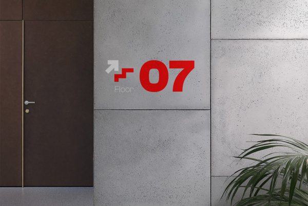 Front view, concrete wall mockup with strong red typography design inside the office and a visible wooden door and stairs behind.