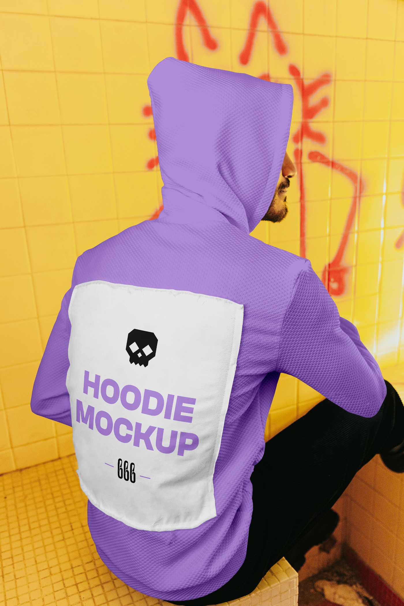A man sitting on a wall with his back to the lens wearing a hoodie mockup with typography design between dirty space area.