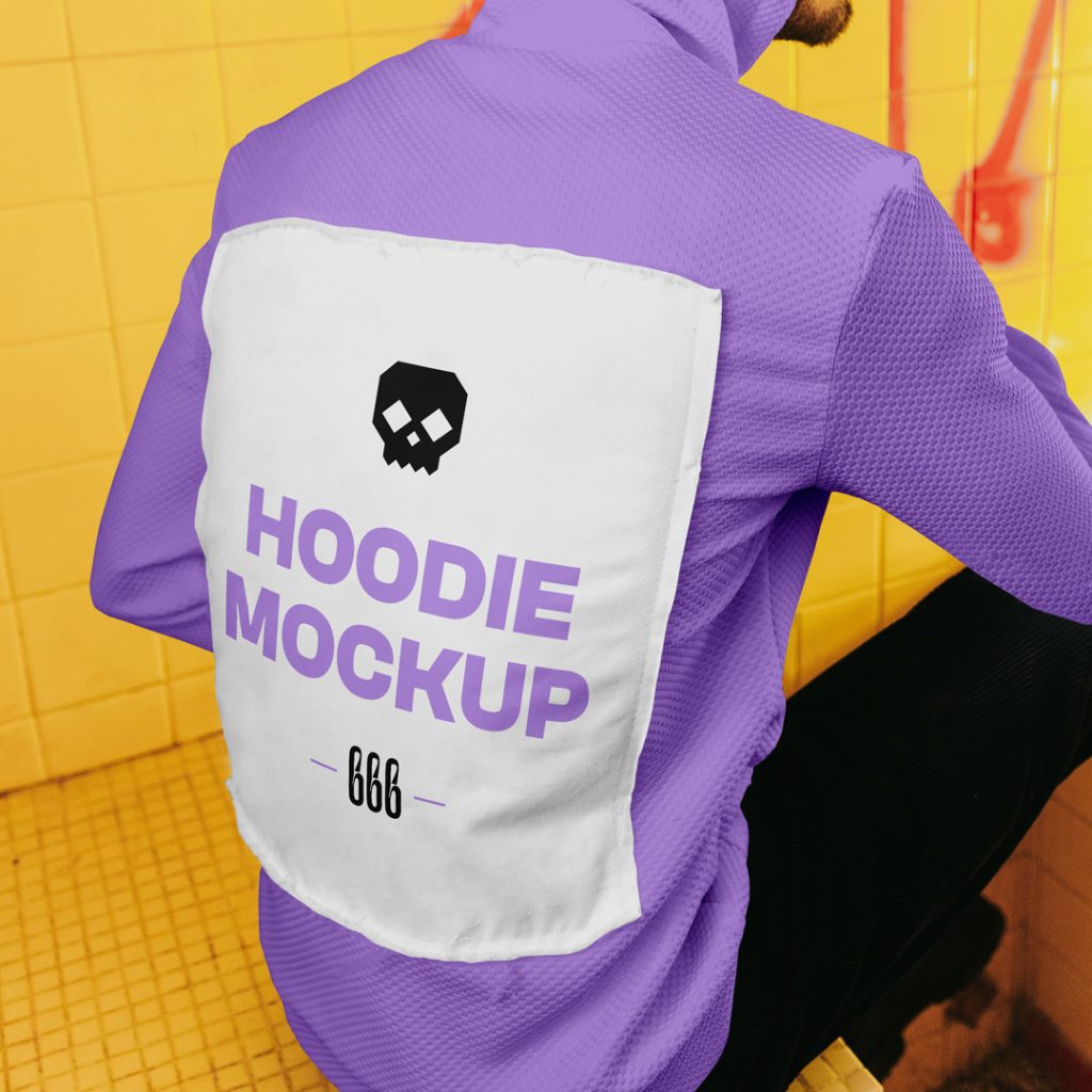 A man sitting on a wall with his back to the lens wearing a hoodie mockup with typography design between dirty space area.