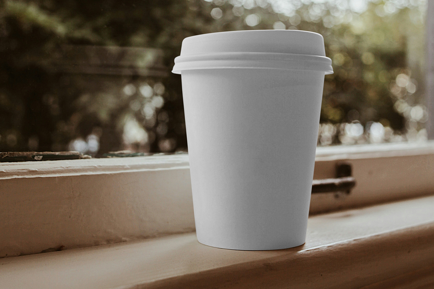 Front view, white coffee cup mockup standing on the windowsill with a window is visible in the background.