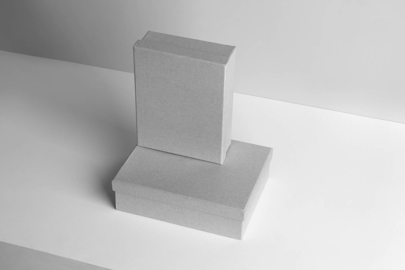 View of two white box mockups lying on top of each other on the white table and visible white color wall in the background.