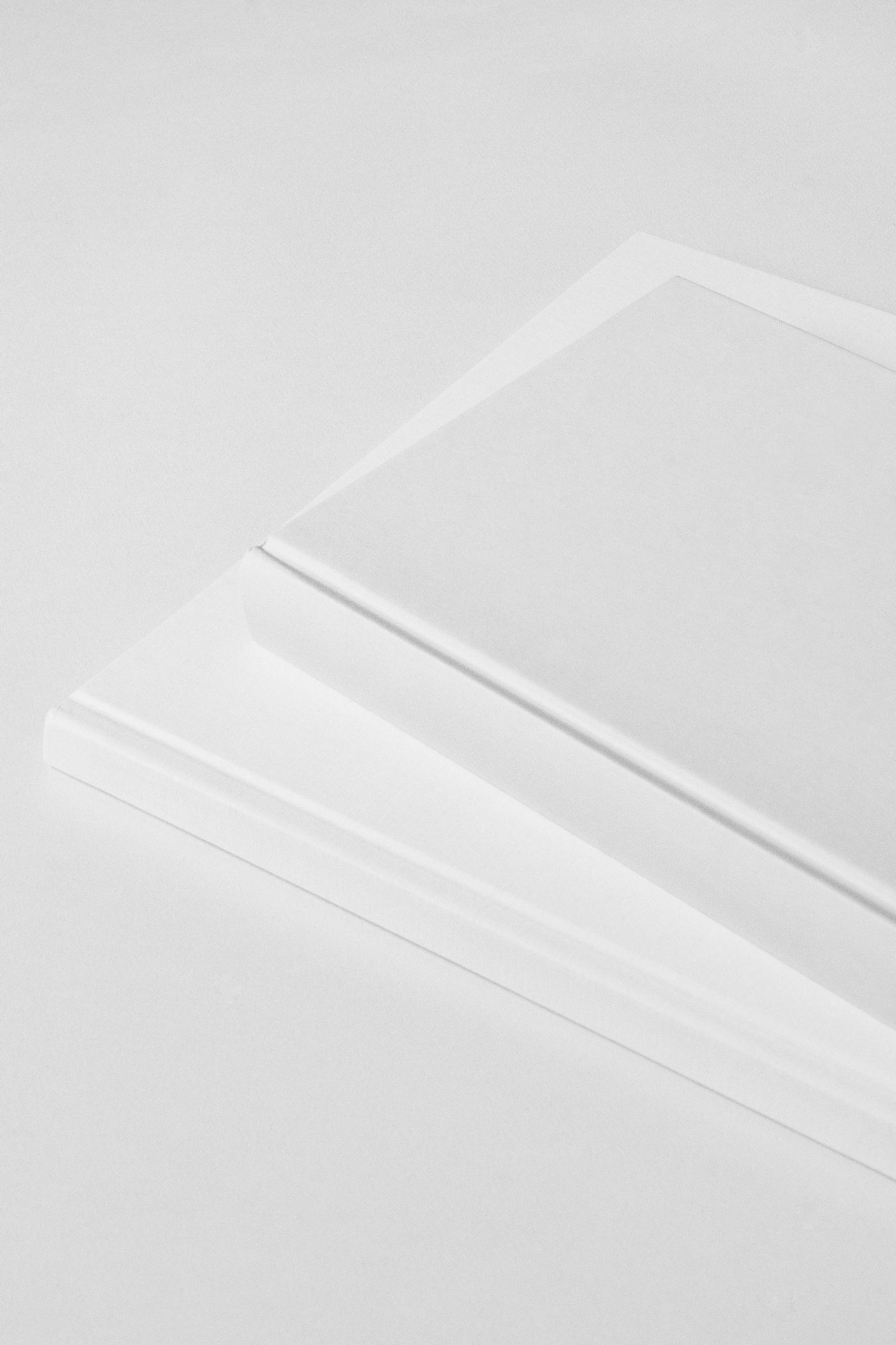 View of two blank hardcover book mockups lying on top of each other on the white floor.