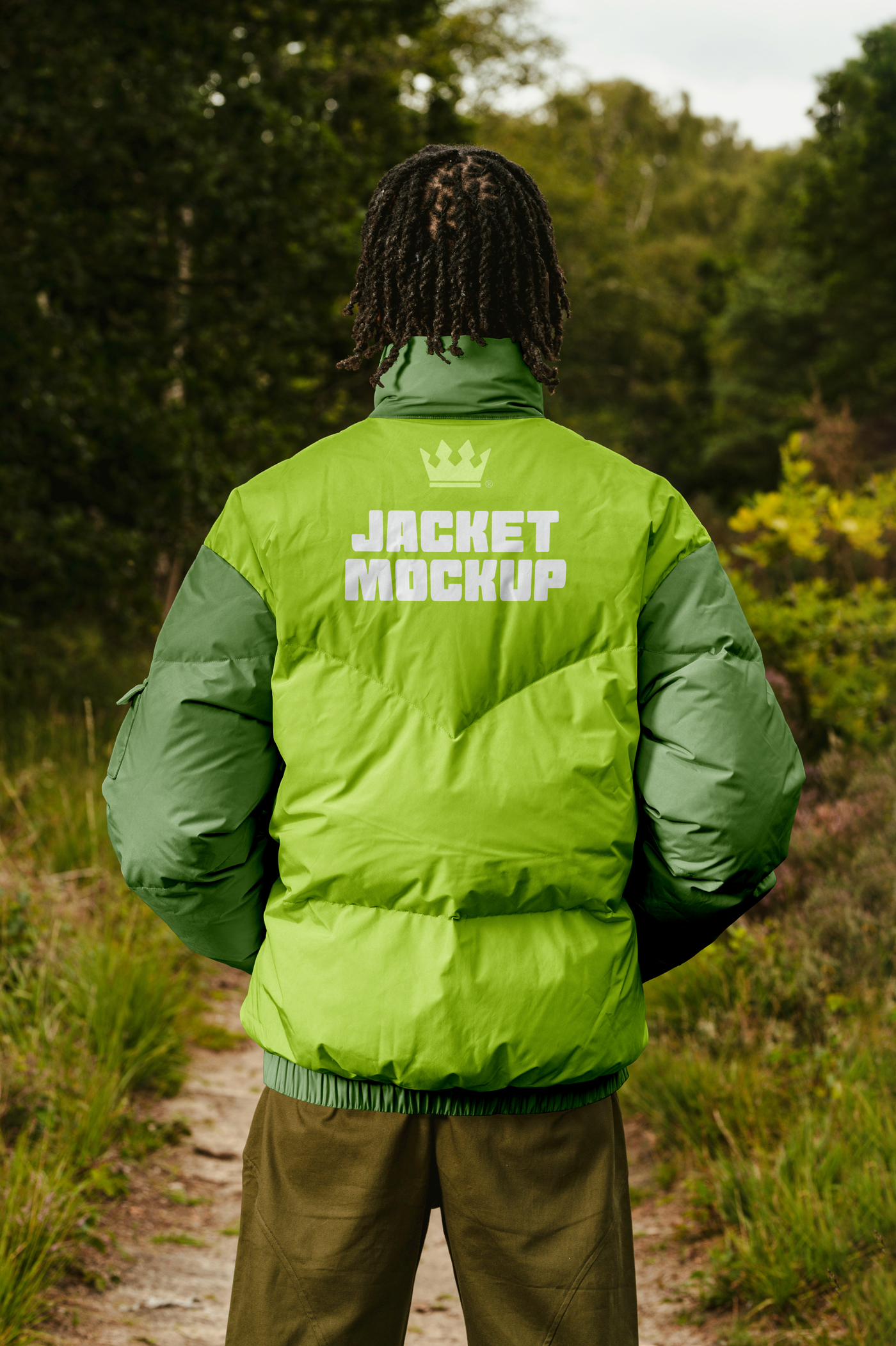 Men standing backward wearing green Winter Jacket Mockup with white strong typography design in the blurred forest in the background.