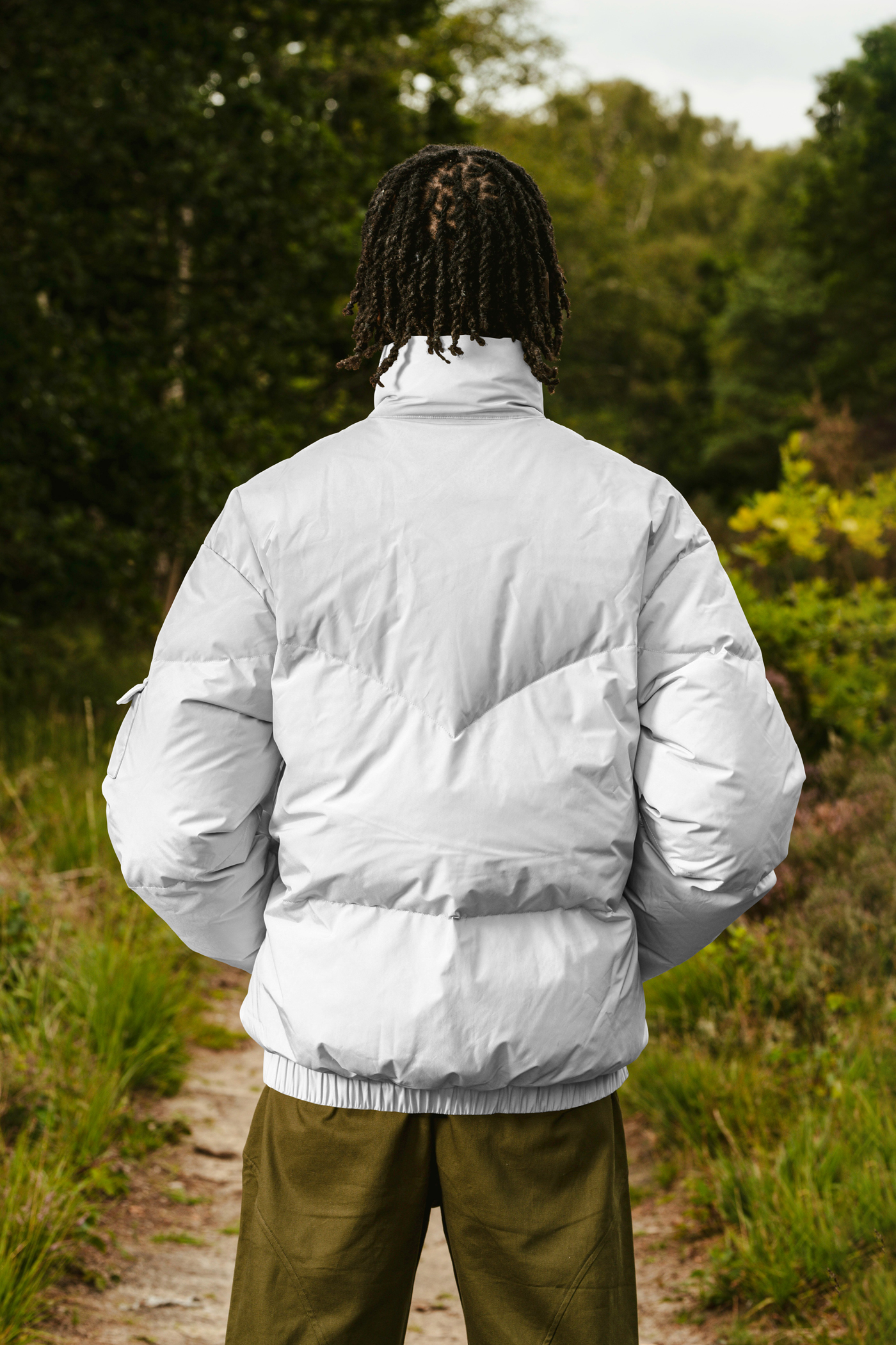 Men standing backward wearing white Winter Jacket Mockup in the blurred forest in the background.
