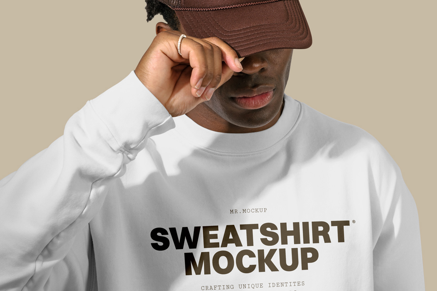 Standing men wearing a White Sweatshirt Mockup with a brown typography logo in front of the beige wall.